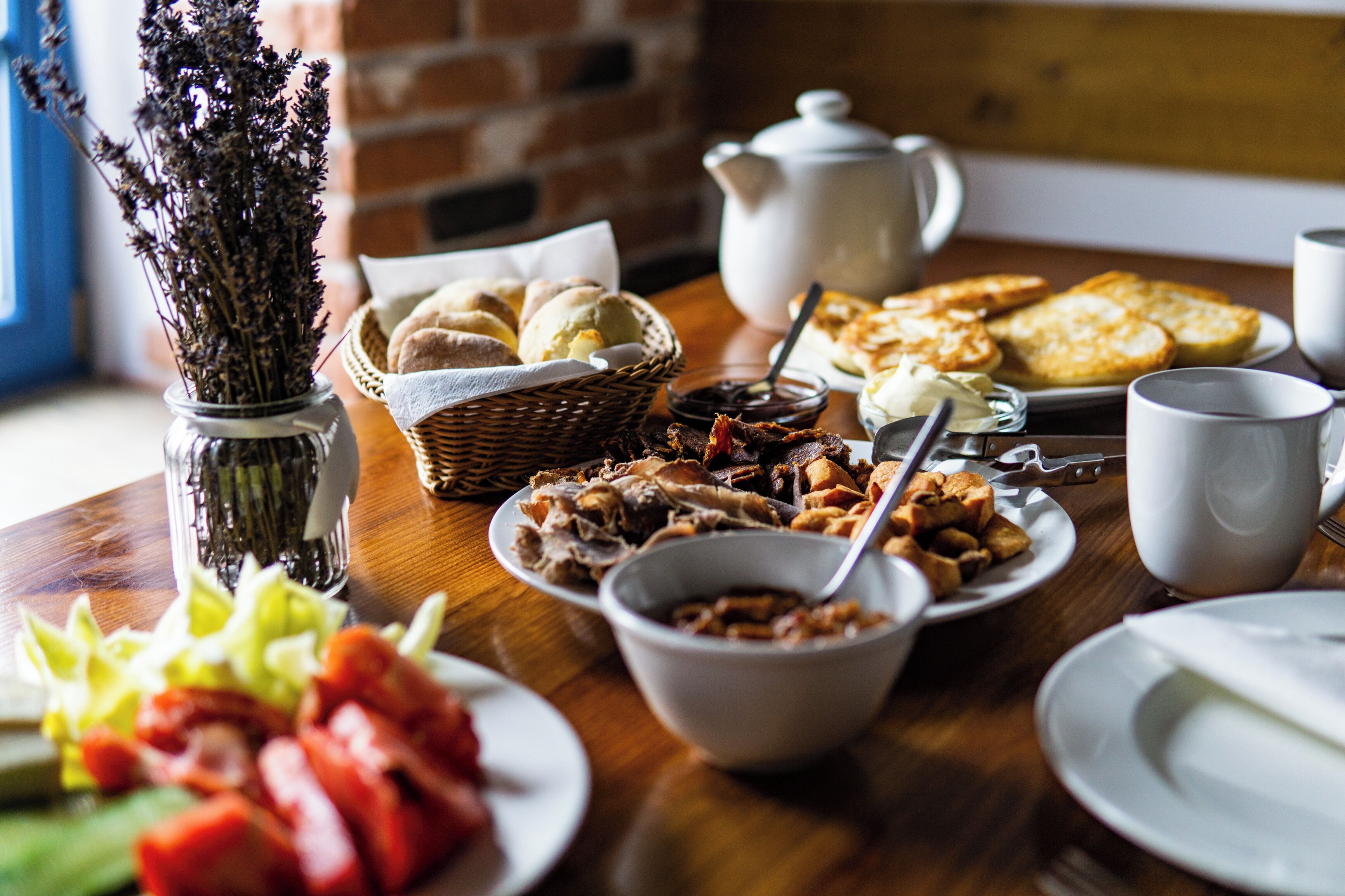 Una mesa de desayuno con diversos alimentos, un jarrón de flores secas y un hervidor de té.
