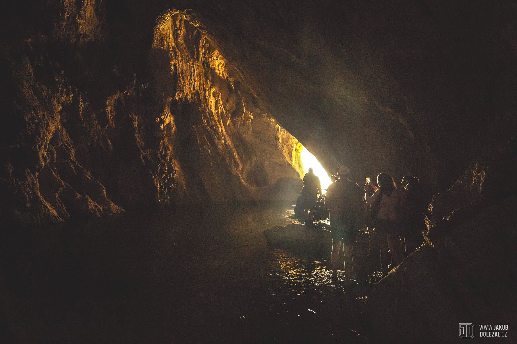 A cave with a bright light source at the entrance, surrounded by rocky walls.
