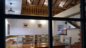 Un comedor con mesas y sillas de madera, una escalera y una cocina visible a través de una ventana.
