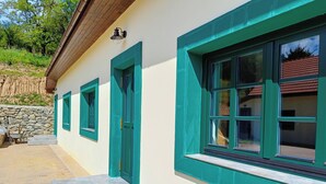 Un edificio con ventanas y puertas enmarcadas en color aguamarina, una pared de piedra y una zona de patio pavimentada.