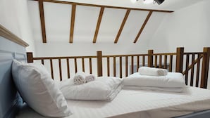 Una cama bien hecha con sábanas blancas y toallas enrolladas, un cabecero de madera y un techo inclinado con vigas a la vista.