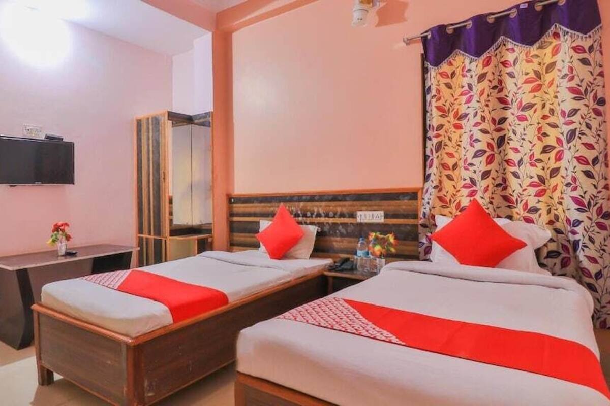 Habitación de hotel con dos camas individuales, un escritorio, un televisor y un espejo.