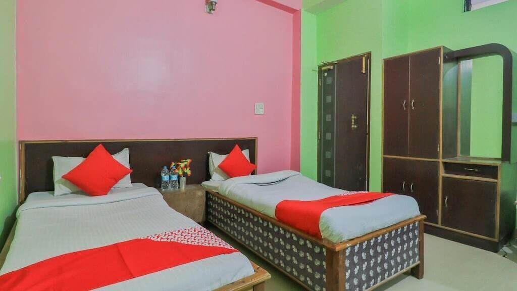 A room with two beds, each with red pillows, a wardrobe, and a mirror.