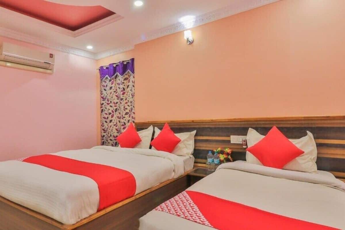 Habitación de hotel con dos camas, cada una con ropa de cama roja y blanca, un ventilador de techo, un equipo de aire acondicionado y una cortina decorativa.