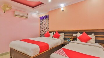 A hotel room with two beds, each with red and white bedding, a ceiling fan, an air conditioning unit, and a decorative curtain.