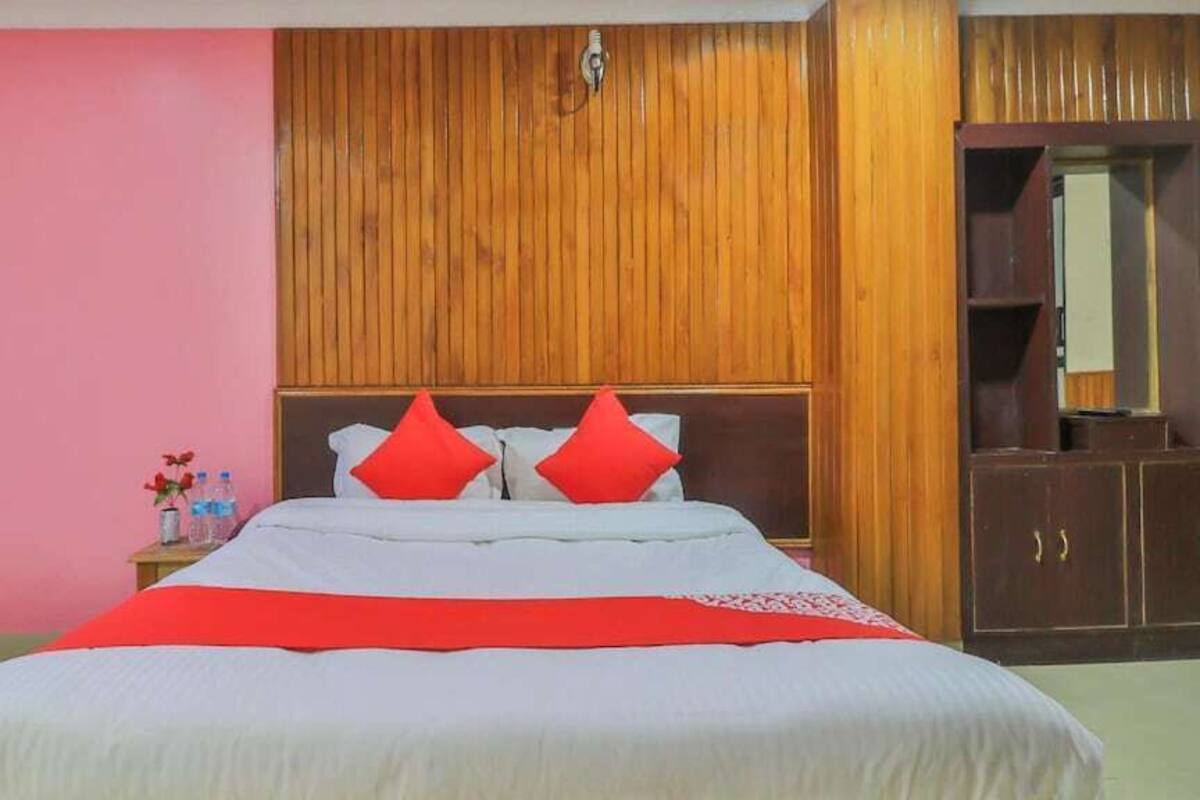 Un dormitorio con cabecera de madera, cama con almohadas rojas y mesita de noche con un jarrón de flores.