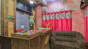 Un área de recepción con un escritorio de madera, un sofá estampado y una ventana con cortinas rojas.