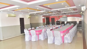 Un salón de conferencias con una larga mesa, sillas blancas y un mantel rosa.