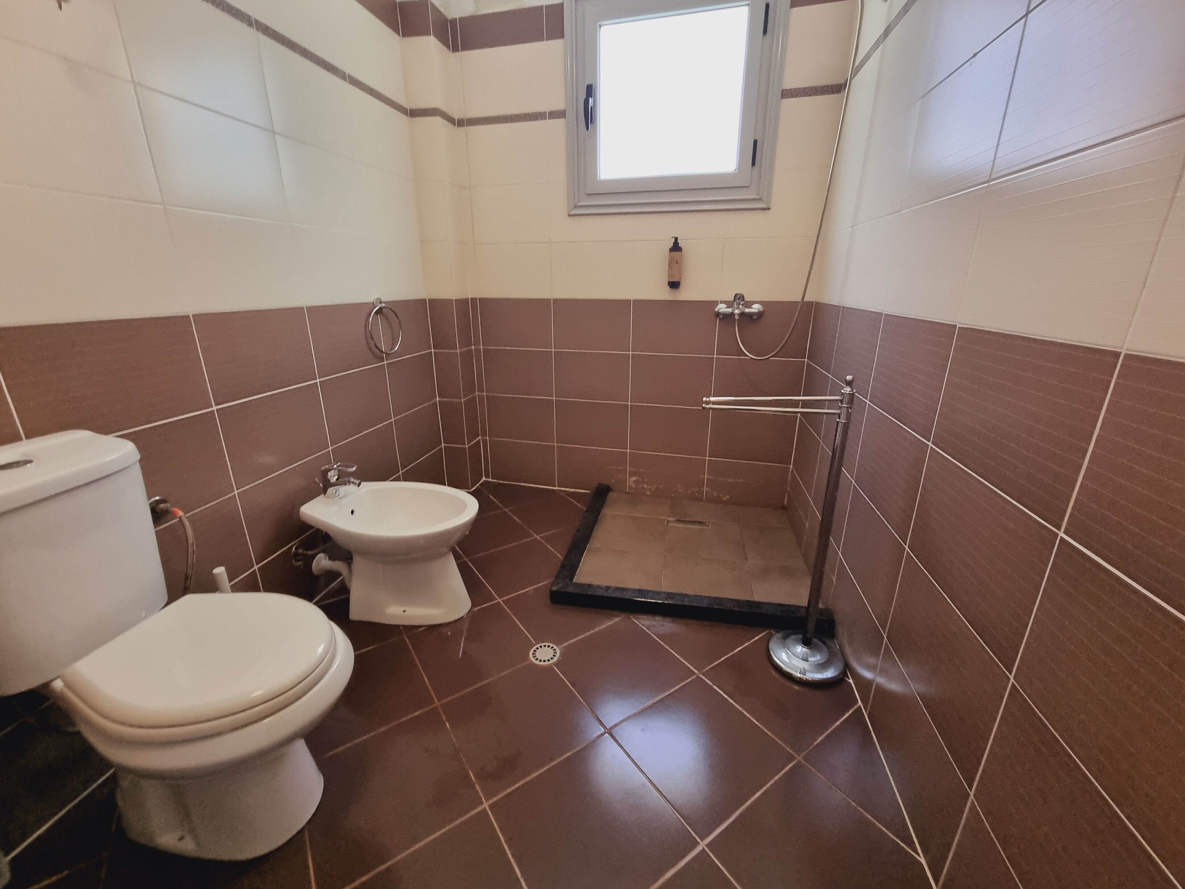 A bathroom with two toilets, a shower, and a window.
