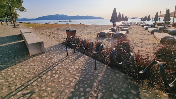 Une promenade en bord de mer agrémentée de chaises longues et de parasols, un sentier pavé et une vue sur la mer et les montagnes.