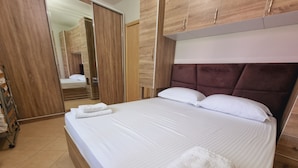 Un lit bien fait, avec du linge de lit blanc et deux oreillers, une armoire en bois et un miroir.
