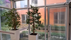 Une véranda avec deux plantes en pot, de grandes fenêtres et une vue sur un immeuble doté de balcons.