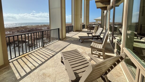 Een balkon met uitzicht op het strand, voorzien van loungestoelen en een tafel.