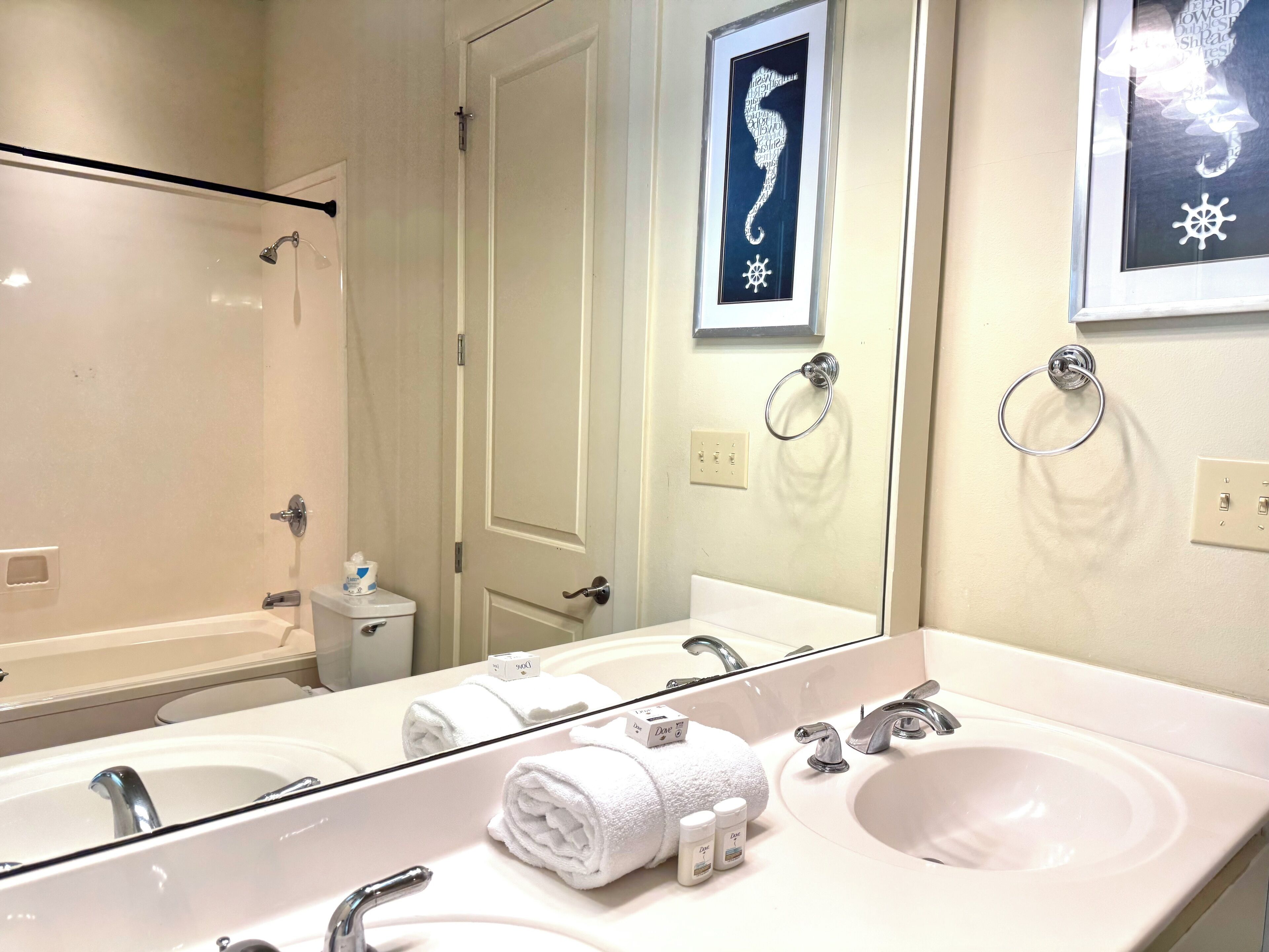 A bathroom with a large mirror, two sinks, a shower, and a toilet.