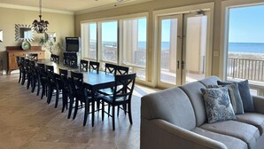 Een ruime eetruimte met een lange tafel en stoelen, een plafondventilator en uitzicht op de oceaan door grote schuifdeuren.