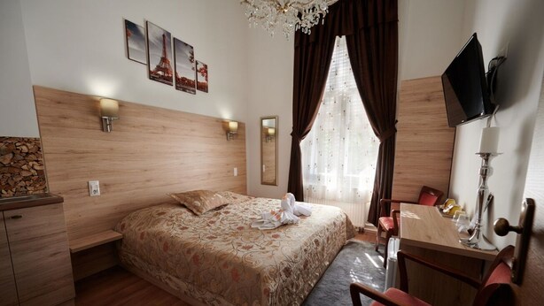 Une chambre d’hôtel avec une tête de lit en bois, un lit avec une literie à motifs floraux, un bureau avec une chaise, une télévision et un miroir.