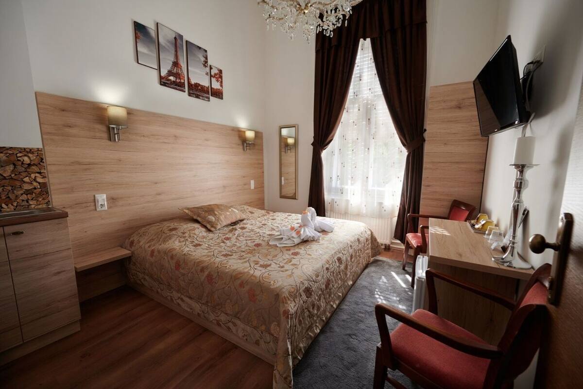 A hotel room with a wooden headboard, a bed with floral bedding, a desk with a chair, a TV, and a mirror.