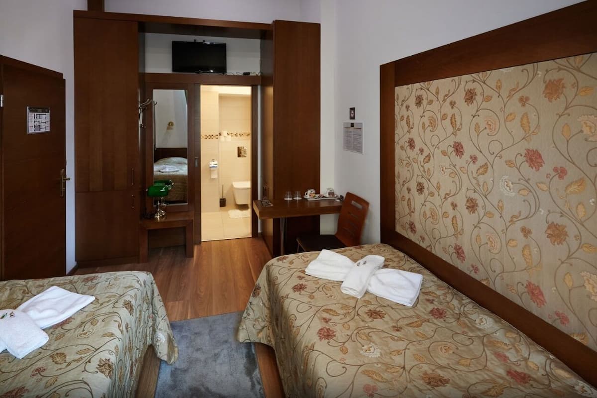 A hotel room with two beds, a desk, a chair, a television, and a bathroom visible through an open door.