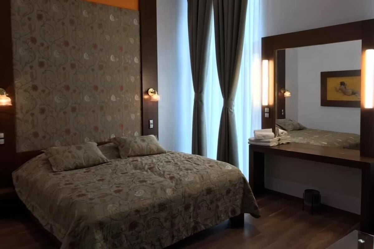 A hotel room with a large bed, a smaller bed, a mirror, and a window with curtains.