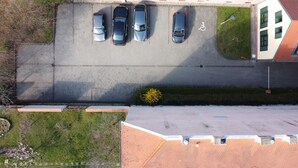Une vue aérienne d’un parking où cinq voitures sont garées à la suite, avec un chemin piétonnier et un bâtiment au toit rouge en arrière-plan.