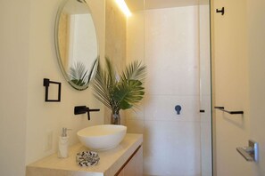 Une salle de bain avec un grand lavabo blanc, un miroir, une petite plante et un espace douche.