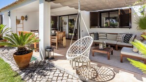 Een terras met een hangstoel, een bank en een eettafel.