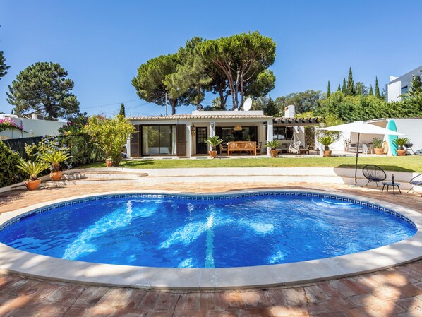 A swimming pool with a tiled edge, surrounded by a patio area with outdoor furniture and potted plants.
