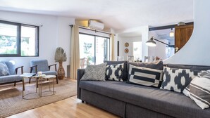 Een moderne woonkamer met een grijze bank, twee fauteuils, een salontafel en een groot raam.