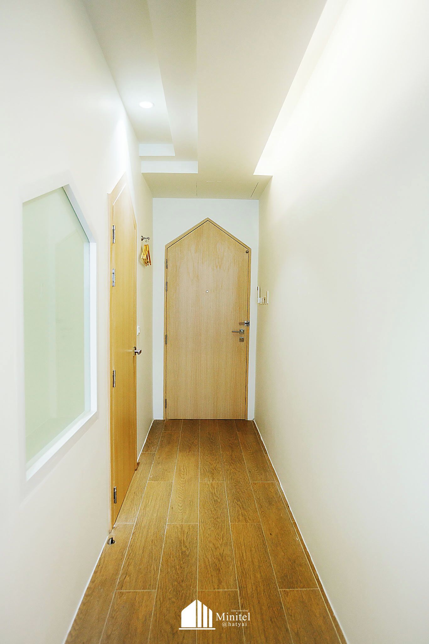 A hallway with a wooden door, white walls, and a wooden floor.