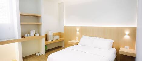 Una habitación de hotel moderna con una cama grande, estanterías empotradas, una mesita de noche y una lámpara fijada a la pared.