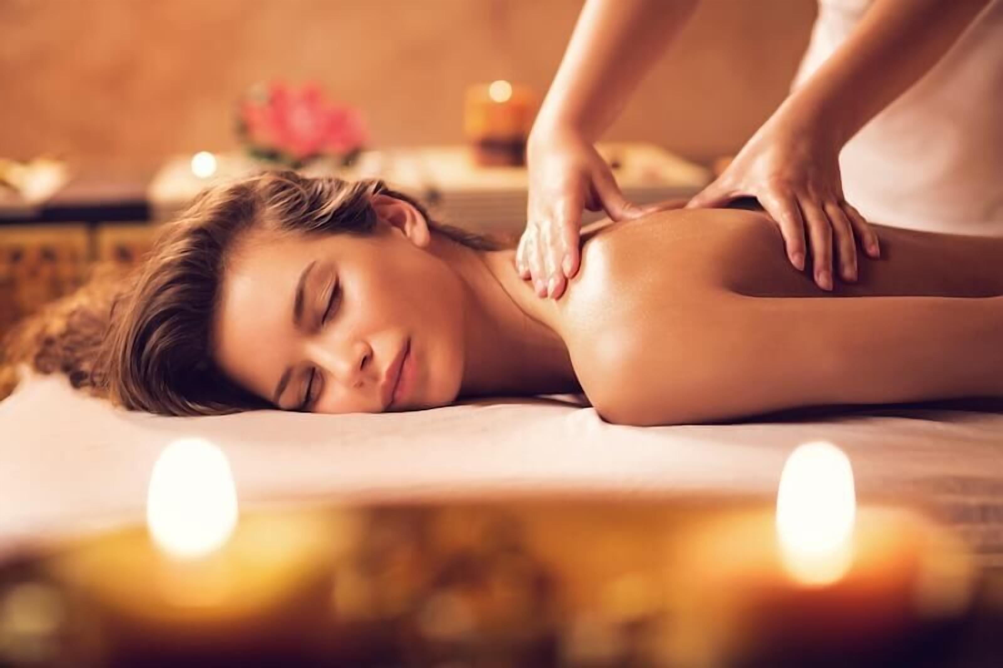 A person receiving a massage on a bed with candles in the background.