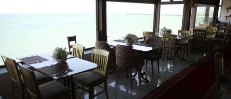 Ein Restaurant mit Meerblick, ausgestattet mit Holztischen und -stühlen und einem roten Teppich.