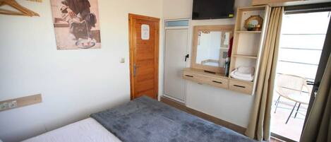 Una habitación de hotel con cama, armario de madera, televisión y un pequeño balcón con una silla.