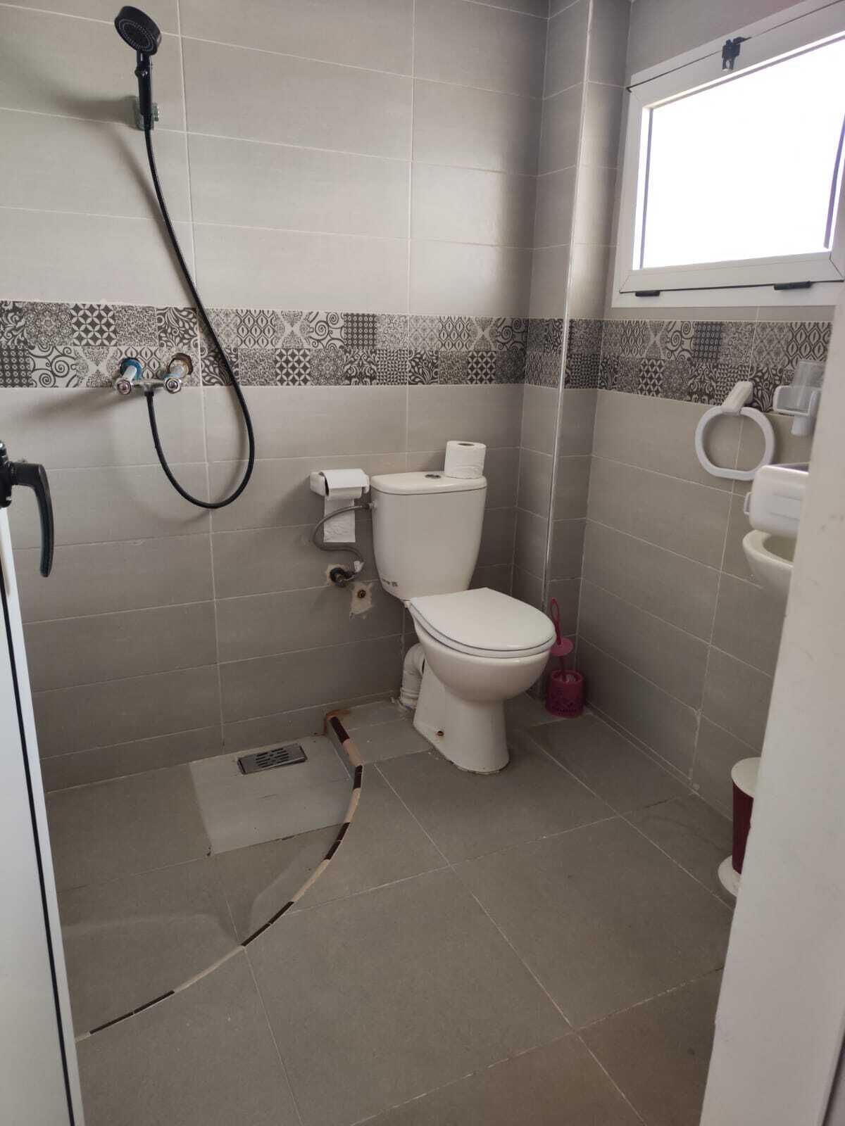A small bathroom with a toilet, a shower, and a window.