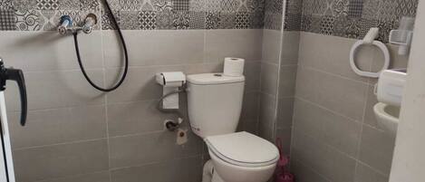 A small bathroom with a toilet, a shower, and a window.