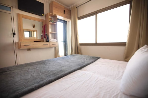 Une chambre d’hôtel avec un lit, une armoire en bois, un miroir et une fenêtre avec des rideaux.