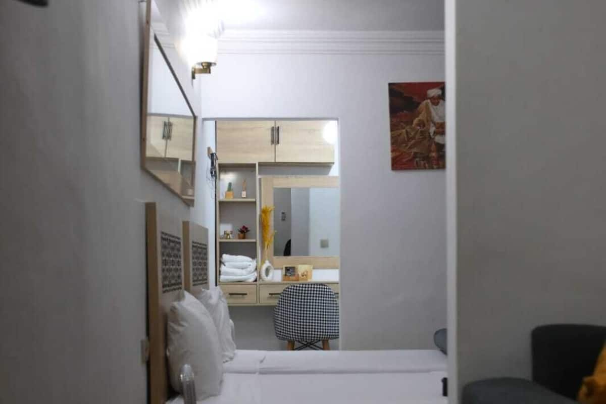 Ein Schlafzimmer mit Bett, Nachttisch und Spiegel. Außerdem ein Sessel und ein kleiner Tisch mit Lampe.