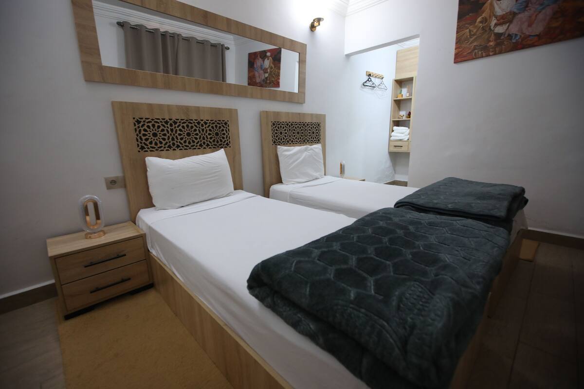 Ein Hotelzimmer mit zwei Betten, einem Holznachttisch, einem Spiegel und einem Bild an der Wand.