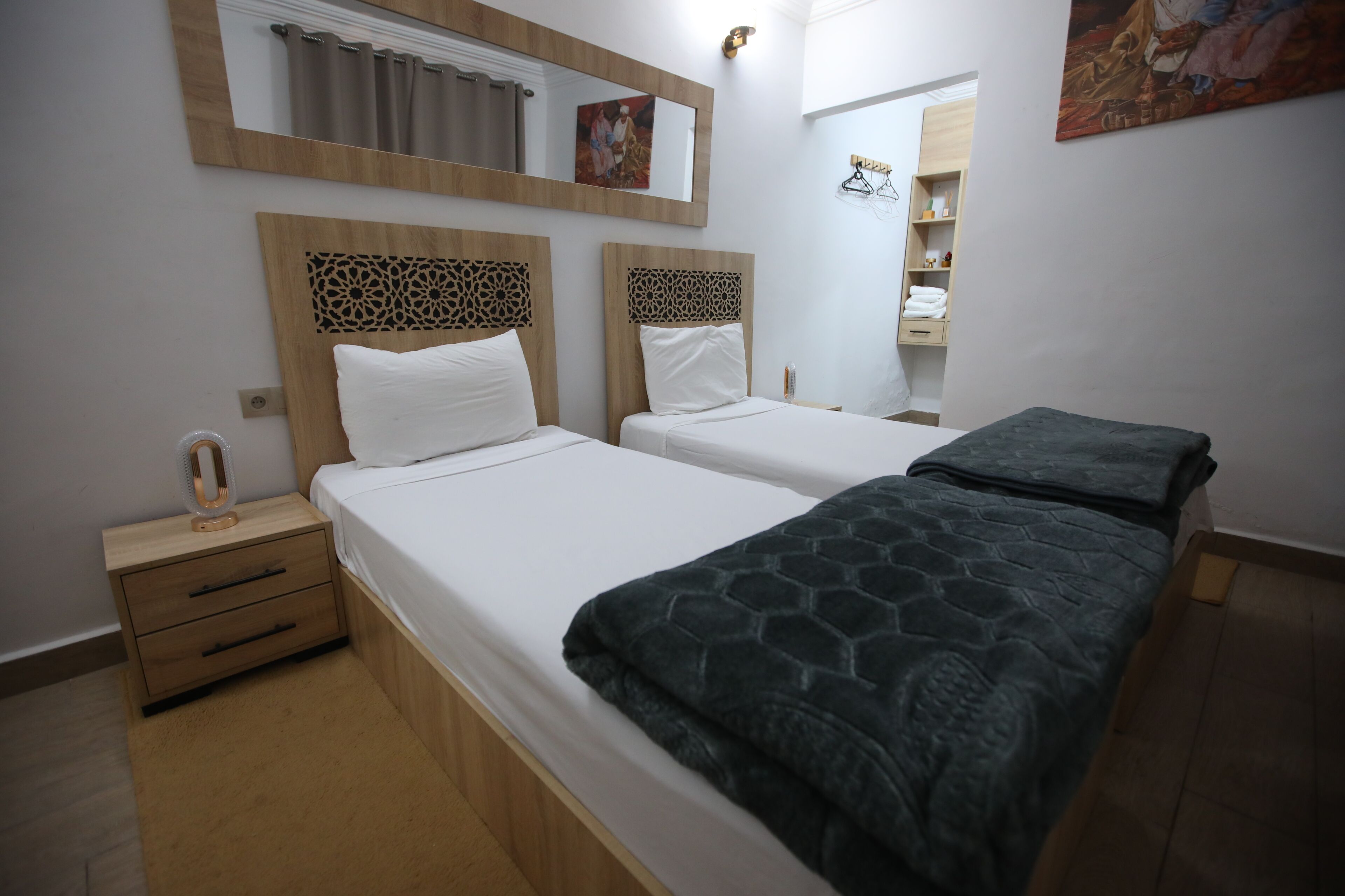 A double bed with a patterned blanket, a nightstand with a mirror, and a wooden headboard.