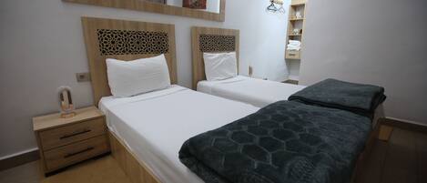 A double bed with a patterned blanket, a nightstand with a mirror, and a wooden headboard.