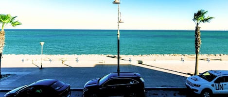 Ein Parkplatz direkt am Strand mit Autos, einer Lampe und Blick auf das Meer.