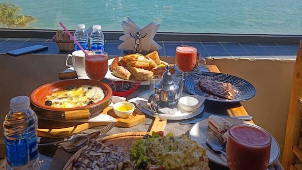 A table set with various dishes and drinks, overlooking a body of water. - HOTEL PLAYA DAKHLA (Dakhla)