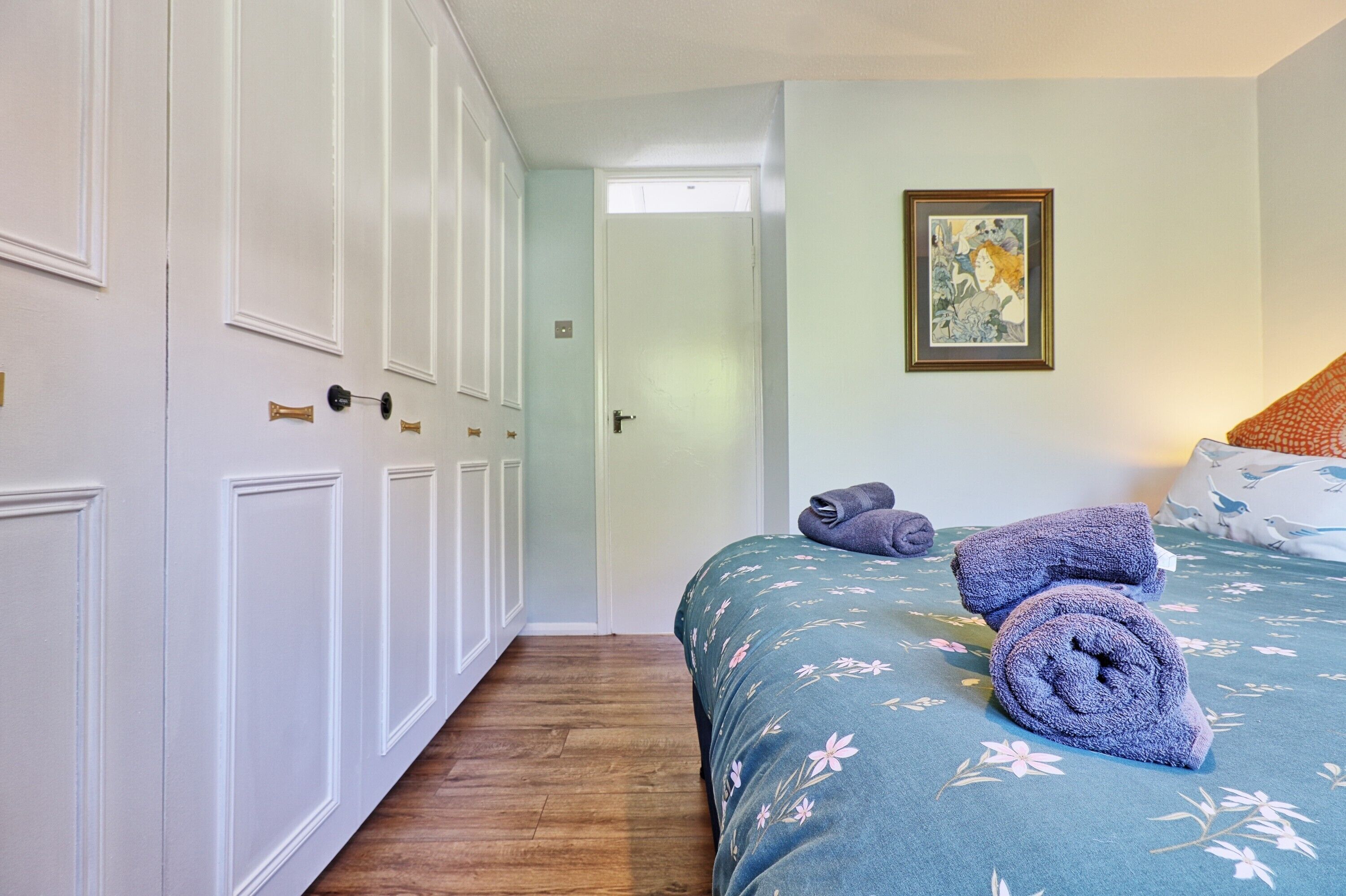 A bedroom with a bed, a door, a framed picture, and a hallway.