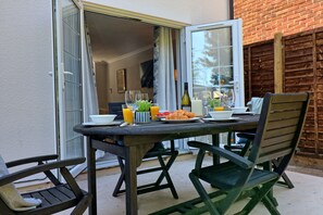 Een buitenruimte met eethoek, een tafel voor twee compleet met een fles wijn, glazen en een croissant.