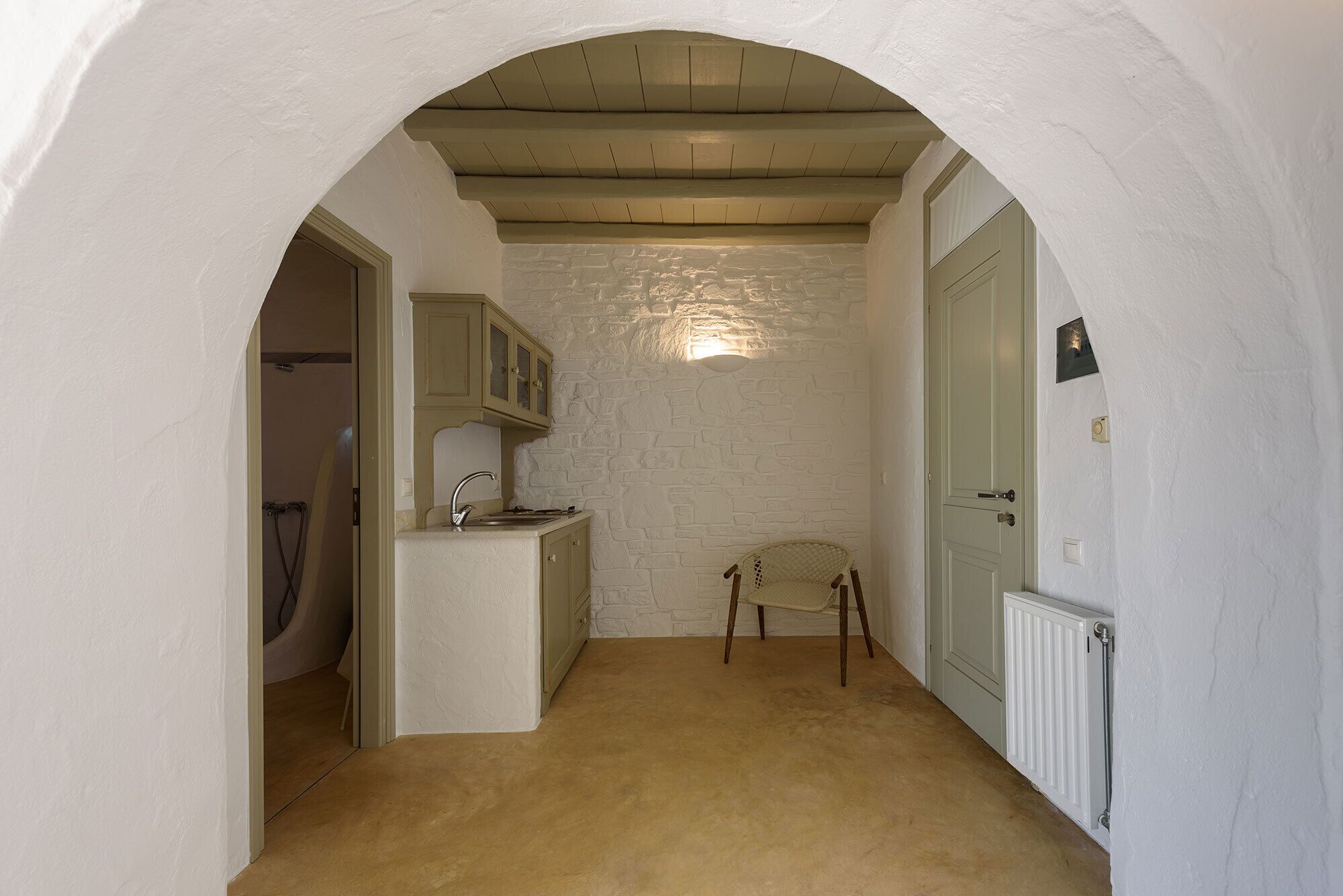 A narrow hallway with a kitchen area featuring a stone wall, wooden cabinets, and a chair.