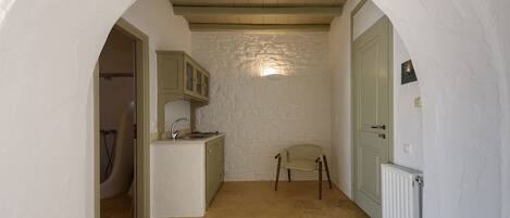 A narrow hallway with a kitchen area featuring a stone wall, wooden cabinets, and a chair.