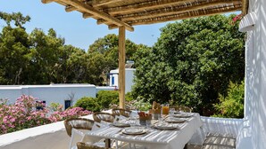 An outdoor dining area with a table set for two, surrounded by wicker chairs, under a pergola. - Villa Vinea Paros (Paros)