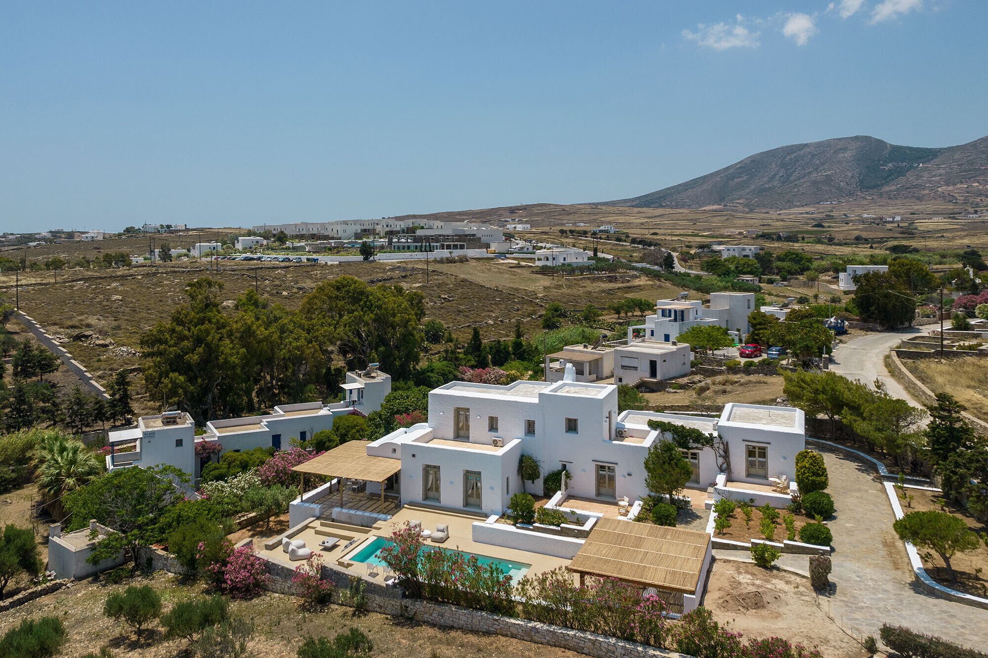 A coastal residential area with white buildings, a swimming pool, and a mountainous backdrop.