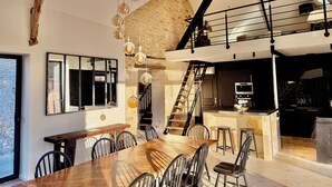 A modern kitchen with a central island, a dining area with a large wooden table and chairs, and a staircase leading to an upper level.