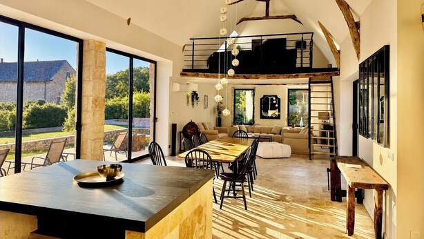 A spacious living area with a dining table, a sofa, and a staircase leading to an upper level.